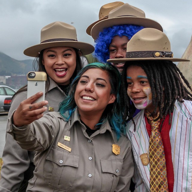 Two new Junior Rangers in clown makeup and wigs pose with rangers for a selfie.
