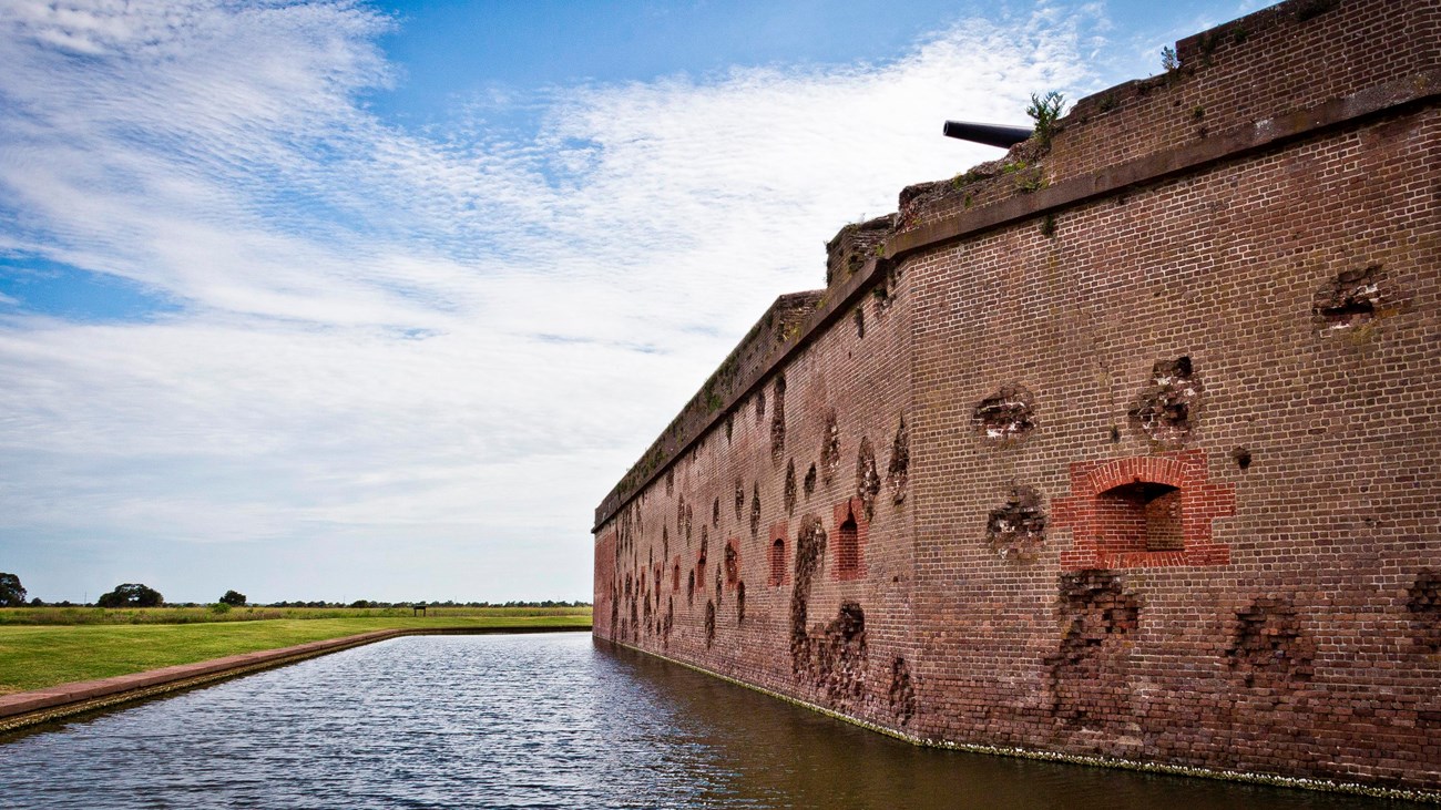 The outside wall of Fort Pulaski with battle scars, cannon, and moat. 