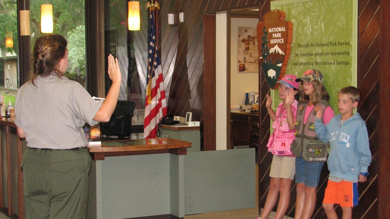 color photo of a ranger standing left swearing in three Junior Rangers standing right