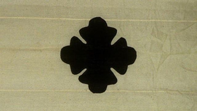 A mostly white/beige flag with a black 4-point star with rounded points. 