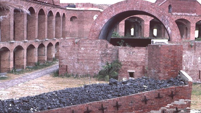 inside a brick fort with archways on the left and bin of coal in foreground