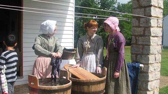 Three laundresses doing laundry while a student looks on.