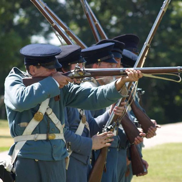 A line of soldiers takes aim with period rifles