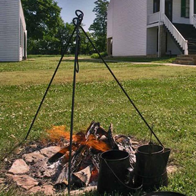 A cooking fire burns in a fire ring on the lawn at Fort Scott