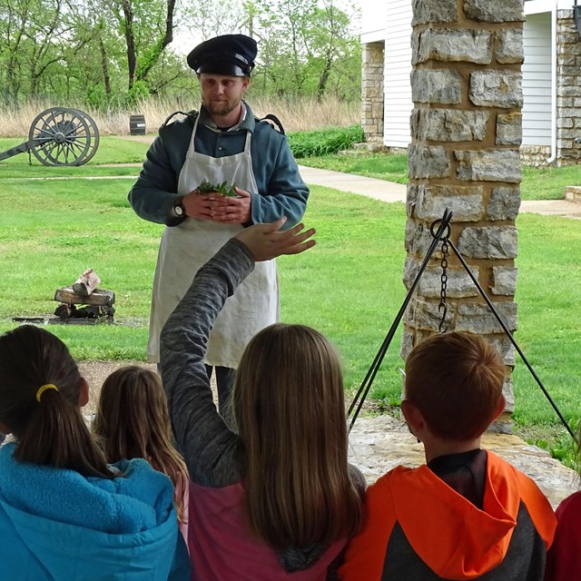 An interpreter holds a bundle of herbs in front of students.