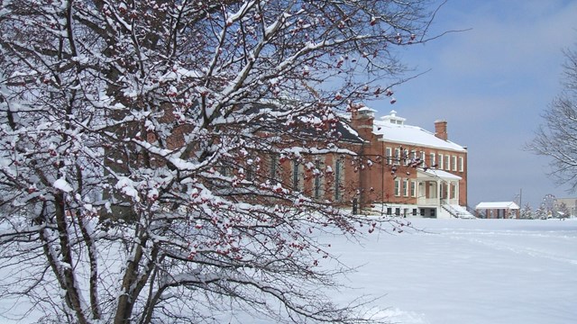 A snow-covered Hawthorn bush partially obscures the red brick visitor center in the background. 