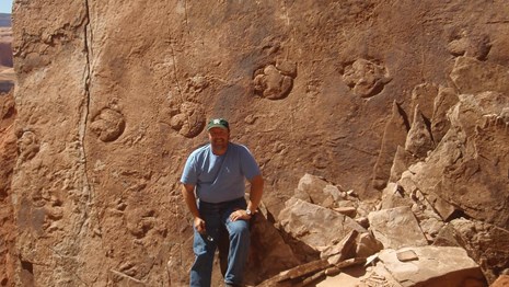 a man standing in front of a large rock slab with fossil tracks