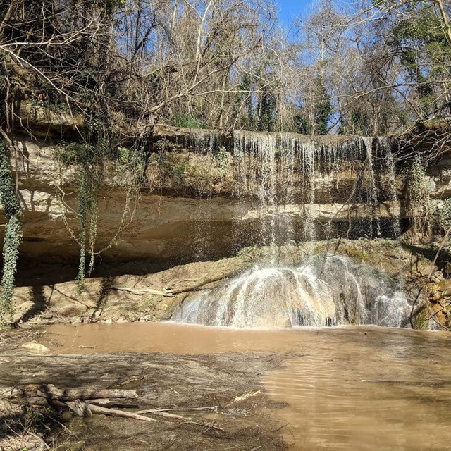 A photograph of a waterfall descending over a rock face made up of a series of beds that are more or