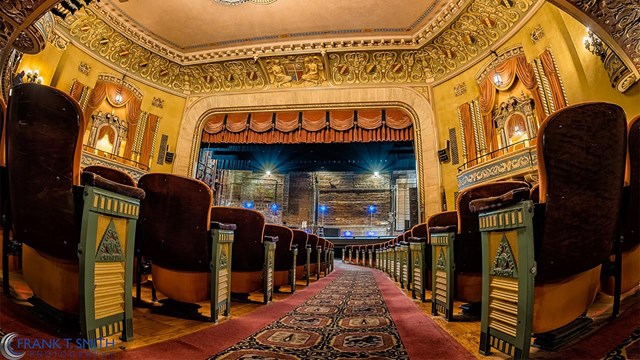 Looking at the stage of a grand, but empty, theater from the aisle. 