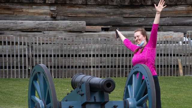 A woman poses next to a cannon, smiling!
