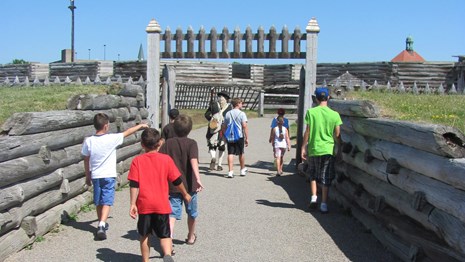 A Continental soldier leads a group of children through the fort gate. 