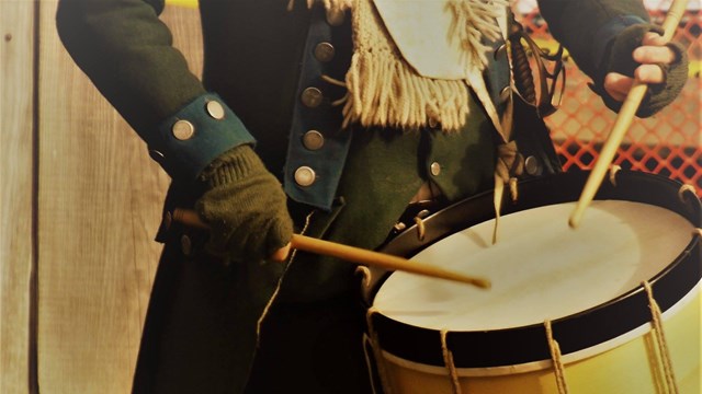 A close up of a large drum at the waist of a soldier. 