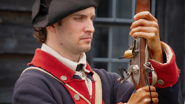 A Continental Soldier stands holding his musket in front of his face