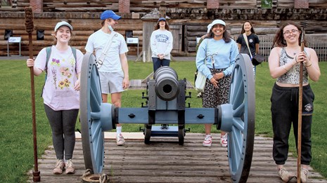 Several young people stand in formation around a cannon holding various cannon implements.