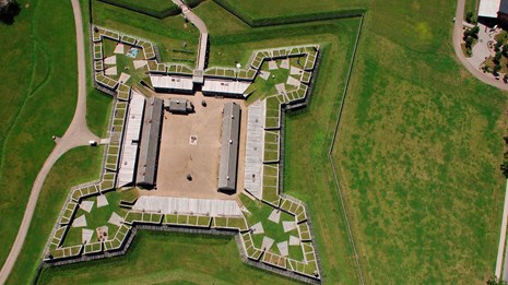A view of the fort from above. A wooden star-shaped building sits in the middle of a grass field.
