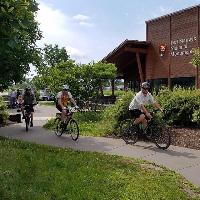 Four cyclists ride the park trail surrounded by greenery. 