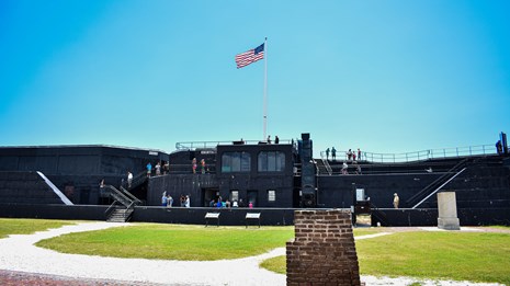 A large black battery on the grassy green parade ground at the Fort. It is a bright blue day.