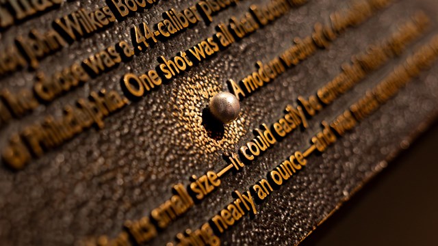 A bronze cast of of a ball rubbed shiny on a plaque with text.