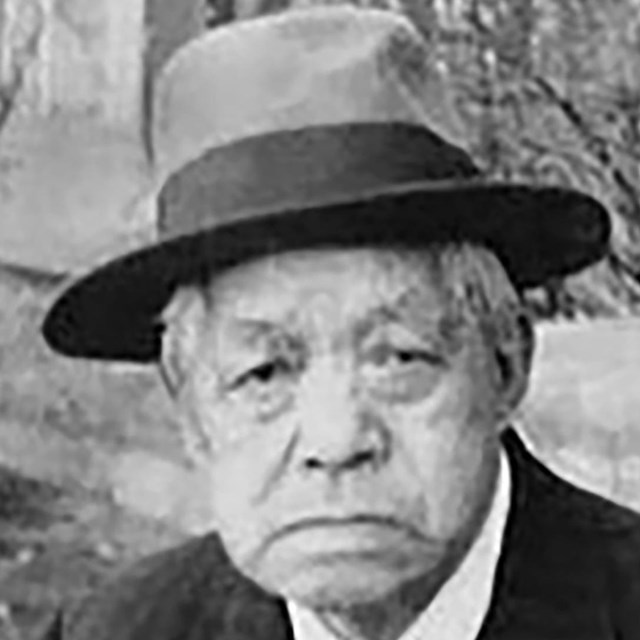 Photograph of older Chinese-Amercan man wearing a fedora and tie and jacket.