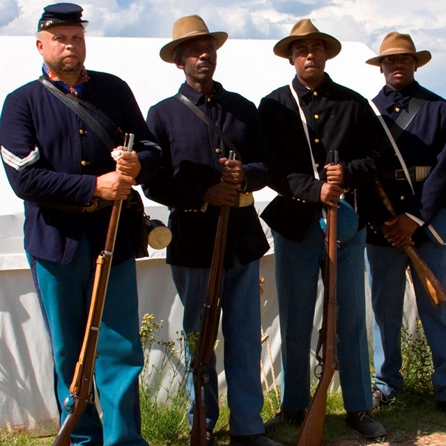 Four African American men standing in a row holding rifles.