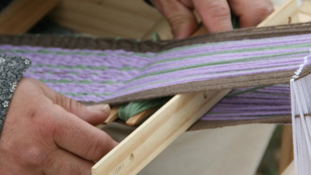 Hands moving a shuttle of yarn through an inkle loom.