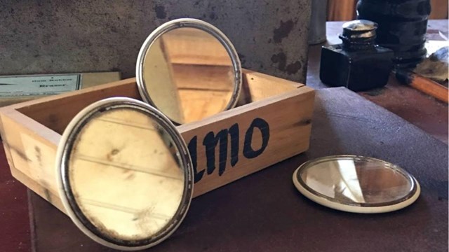 Wooden box reads U.M.O, three small round mirrors placed around with FUA Logo in foreground
