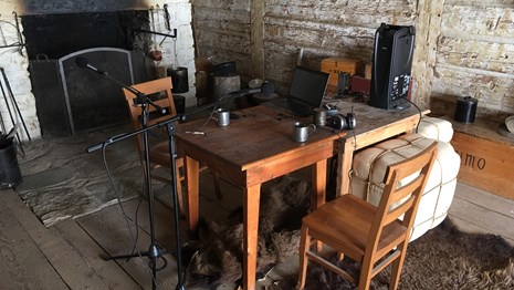 Wooden table with recording equipment in front of large fireplace