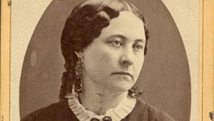 A black and white portrait of a woman wearing a high-collared dress.