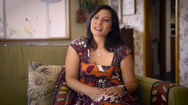 An image of a woman with shoulder length dark hair sitting indoors.