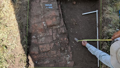 An archaeologist measuring an excavation unit.