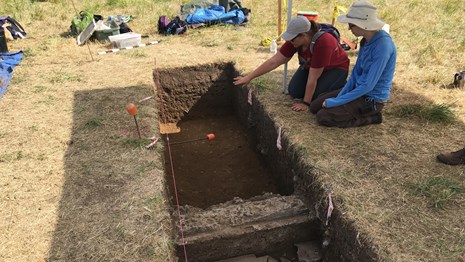 Two archaeologists look at a long archaeological unit.