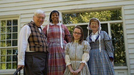 A group of men, women, and a girl wearing 1840s style clothing in front of the McLoughlin House.
