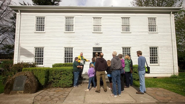 A large tour group led by a docent stands in front of the McLoughlin House.