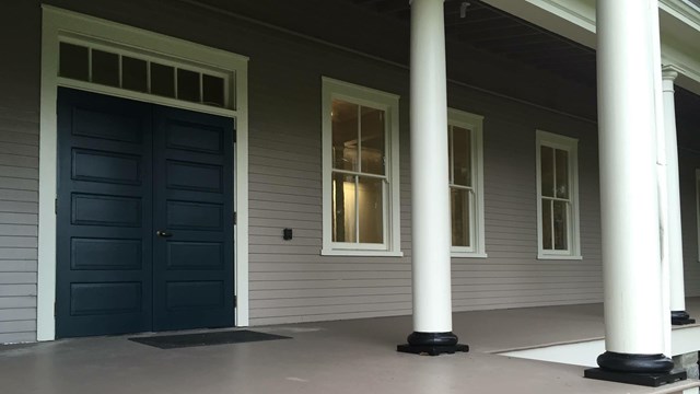 A porch in front of a building leading to a door that is painted blue.