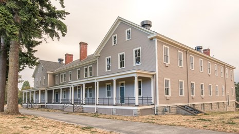 A large two-story barracks building at Vancouver Barracks. It is painted gray with white trim.