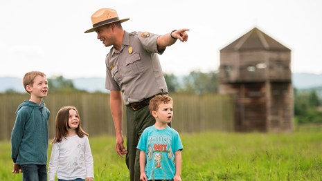 A park ranger stands in the field north of Fort Vancouver with a group of children.