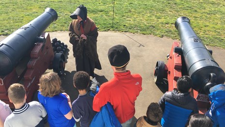 A woman in 1840s clothing talking to a group of students at Fort Vancouver.