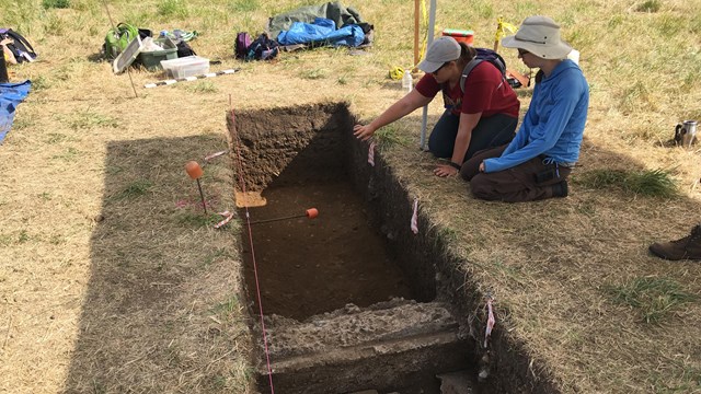 Two archaeologists look at an excavation unit.