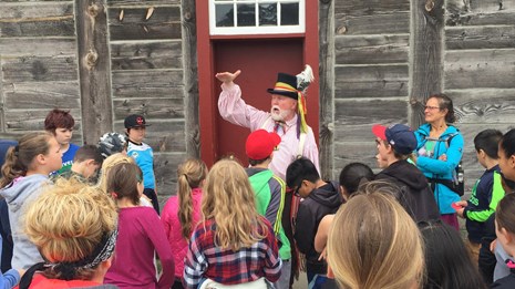 A volunteer dressed as a fur trader talks to a group of students.