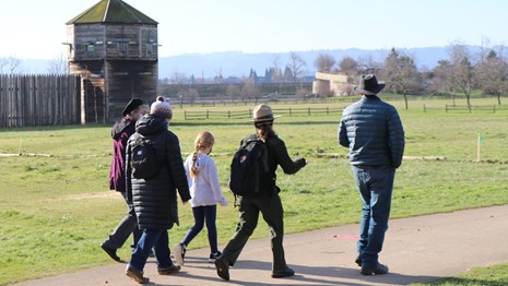 A park ranger walks with a family on a trail outside the Fort Vancouver stockade on a sunny day.