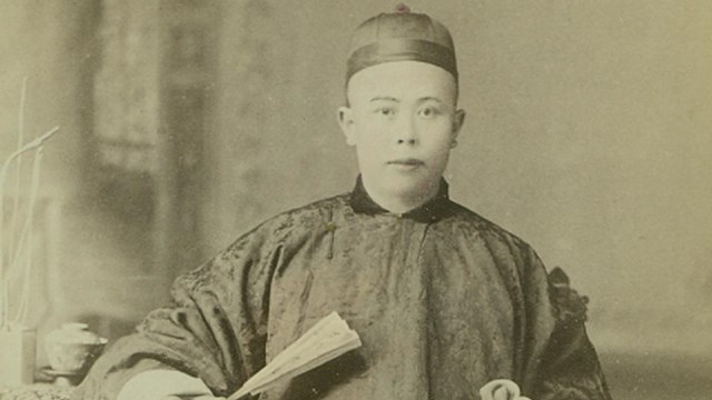 A Chinese man wearing traditional dress in a portrait studio, ca. 1890.
