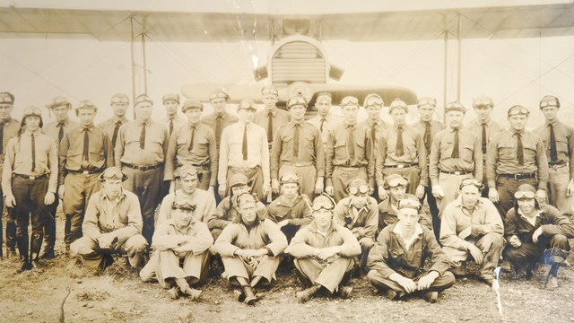 Black and white photograph of sitting and standing men in uniform.