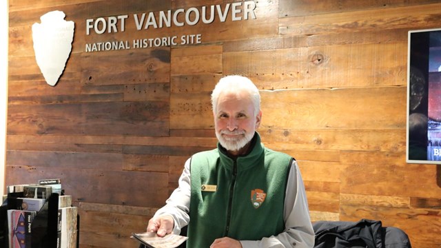 A volunteer dressed in grey and green handing out a Fort Vancouver brochure.