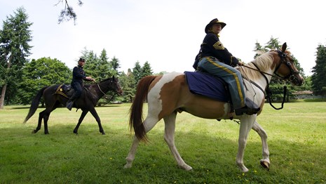 Costumed re-enactors dressed as 19th century US Army soldiers ride horses at Fort Vancouver NHS