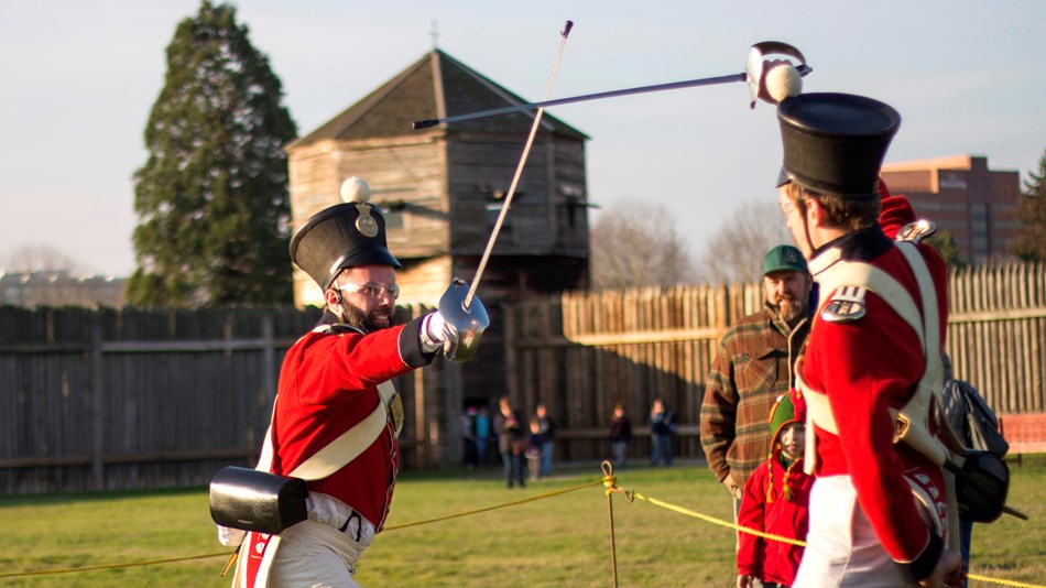 Photo of two reenactors wearing military uniforms and drilling with sabers