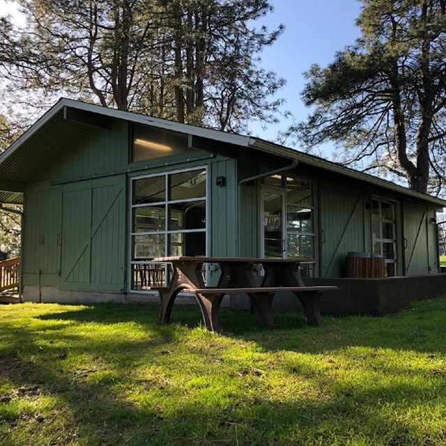 A green building with large windows and picnic benches outside.