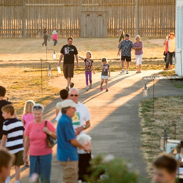 Visitors walk through the reconstructed fort at dusk.