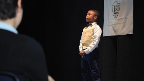 A young student gives a speech from a stage