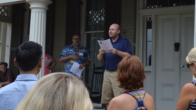 A man reads a speech from the front porch of a historic house
