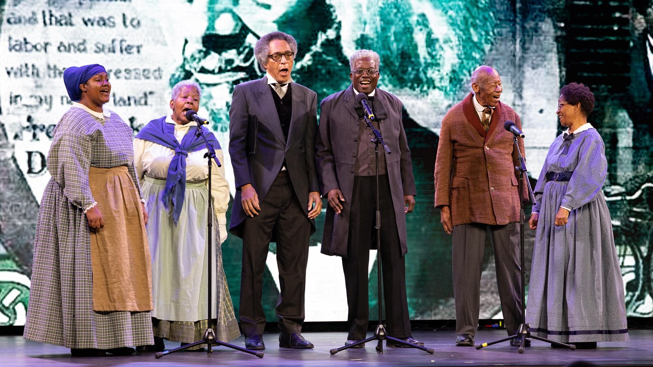 A group of six singers perform on a stage.